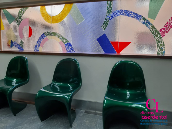 Sala de espera de la segunda planta con sus sillas para la espera del paciente y detras una vidriera con dibujos de colores
